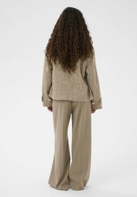 Bež jesenasti volneni blazer s širokimi rokavi in zlatimi gumbi, v kombinaciji z visokim pasom bež širokimi hlačami.