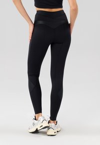 Sorte høye leggings med glatt tekstur, paneldetaljer på sidene, og kombinert med lysegrå treningssko.