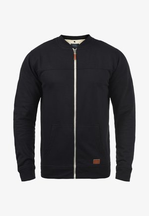 Hanorac cu fermoar de culoare bleumarin, confecționat dintr-un material moale, având un guler înalt, două buzunare frontale și o mică etichetă din piele cu logo la tiv.