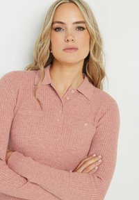 Ribbade långärmade polo i dämpad rosa med krage, fyraknapps placket och två bröstfickor med matchande knappdetaljer.