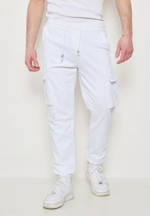 Pantalons cargo blancs dotés de plusieurs poches latérales, d'une taille élastique avec cordon de serrage et d'une coupe fuselée. Assortis à des baskets blanches.
