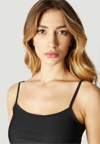 Black tank top with thin straps, made of smooth fabric, featuring a scoop neckline and a fitted design. Skin is visible at shoulders and neck area.