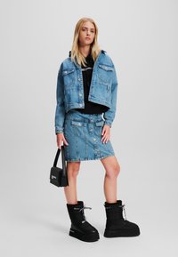 Denim jakna in krilo v svetlo modri barvi z gumbi, v paru s črnimi platform čevlji in črno torbico. Gladka tekstura.