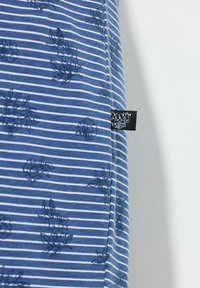 Modrá pruhovaná látka s květinovým vzorem, textury v námořnické a bílé barvě. Malá černá etiketa viditelná na okraji.