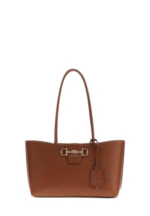Brązowa torba typu tote Guess ze skóry, z podwójnymi uchwytami, srebrną klamrą oraz zawieszką z wytłoczonym logo marki i rokiem założenia.
