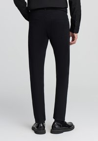 Czarne dopasowane dżinsy o gładkiej fakturze, z czterema kieszeniami i paskiem z pętelkami, w połączeniu z czarnymi eleganckimi butami.