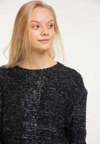 Schwarzer und grauer Strickpullover mit einem strukturierten Zopfmuster auf der Vorderseite, Rundhalsausschnitt und lockerer Passform. Weiches, voluminöses Material.