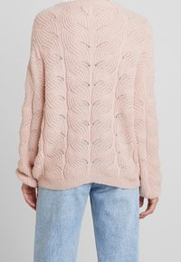 Ljusrosa stickad tröja med kablar, rund halsringning och ribbat avslut. Har lös passform och långa ärmar. Bärs över ljusblå jeans.