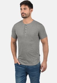 Grå kortærmet henley-shirt med tekstureret finish, fem-knaps placket og subtilt spottet mønster, parret med blå denim jeans.