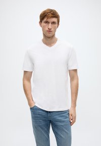 Άσπρο T-shirt με λαιμόκοψη σε σχήμα V, κατασκευασμένο από βαμβάκι, με κοντά μανίκια και χαλαρή εφαρμογή, συνδυασμένο με τζιν παντελόνι ανοιχτού μπλε χρώματος. Απλός σχεδιασμός, χωρίς ορατά μοτίβα ή διακοσμητικά στοιχεία.