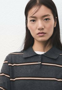 Polo antracite con colletto piatto, caratterizzata da strisce orizzontali in marrone, bianco e arancione. Design con abbottonatura a due bottoni.