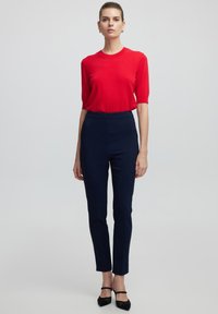 Top rojo de manga corta combinado con pantalones ajustados azul marino, con una textura suave, corte sencillo y zapatos de tacón negros.
