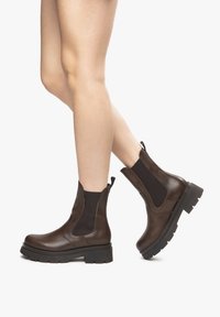 Bottines en cuir brun avec des panneaux élastiques sur les côtés et une semelle épaisse noire. Présente une texture lisse avec un design épuré.