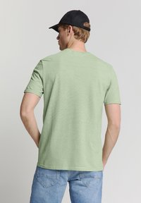 Groene gestreepte T-shirt met korte mouwen en een ronde hals, gemaakt van lichtgewicht stof, gecombineerd met lichtblauwe denim shorts.