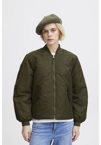 Veste bomber vert olive avec une fermeture éclair sur le devant, des poignets côtelés et deux poches latérales. Matériau doux et texturé ; coupe oversize.
