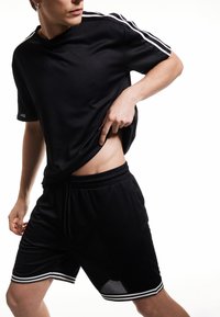 Tenue de sport noire comprenant un t-shirt à manches courtes et un short, avec des rayures blanches le long des épaules et de l'ourlet, fabriquée en matériau respirant.