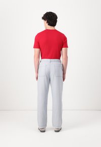 Camisa corta roja de mangas cortas combinada con pantalones sueltos de cintura elástica en gris claro, que cuentan con dos bolsillos traseros y puños ajustados.
