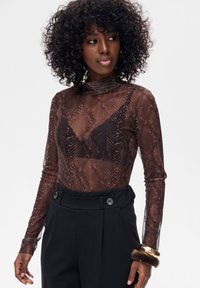 Brązowy przezroczysty top w zwierzęcy wzór z długimi rękawami i wysokim kołnierzem. Do tego wysokie, czarne spodnie z dekoracyjnymi guzikami.