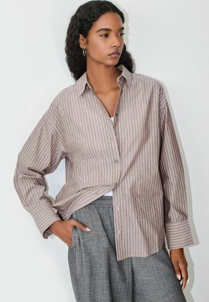 Light brown and cream striped button-up shirt with a relaxed fit and long sleeves, paired with gray trousers. Features a pointed collar and side pocket.