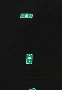 Sort strikket stof med to grønne broderede pengesymboler. Designet inkluderer detaljelinjer omkring symbolerne og en glat tekstur.