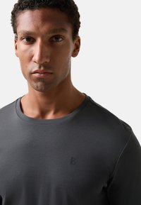 Tmavě šedé tričko s kulatým výstřihem, vyrobené z měkké látky. Na levé části hrudi má malé vyražené logo.