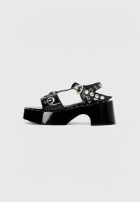 Sandali platform in pelle verniciata nera con design perforato, borchie metalliche e occhielli, dotati di un tacco spesso e punta aperta.