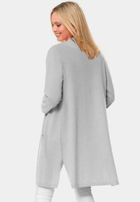 Lange grijze cardigan gemaakt van zachte stof, met een comfortabele pasvorm, open voorkant en zijzakken. Het ontwerp heeft minimale stikdetails.