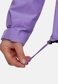 Manga de chaqueta morada con puño fruncido, que presenta un cordón y un tope. Textura suave con un sutil patrón de cuadrícula. Mano sujetando el cordón.
