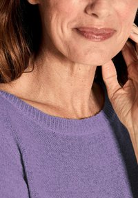 Paarse gebreide trui met een brede halslijn, met een gevarieerde afwerking. Close-up van een vrouwenhals en kin, met zachte haren op de achtergrond.
