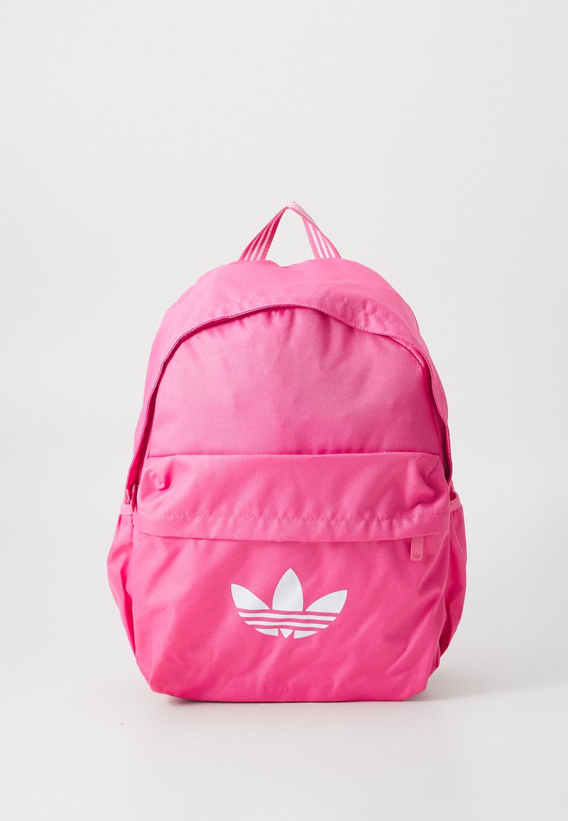 Mochila de tecido rosa com forma arredondada, apresentando um bolso frontal e um design de logótipo branco. Alças ajustáveis com padrão às riscas.