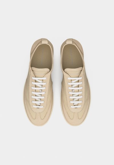 Poros smėlio spalvos laisvalaikio sportinių batelių su baltomis batų raištelėmis, apvaliais noseliais ir minimaliais siūlais, parodytų iš viršaus ant balto fono.
