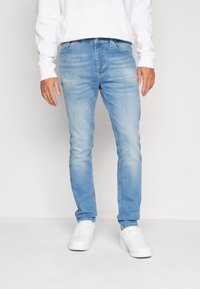 Világoskék, slim fit farmernadrág finom kopással. Denim anyagból készült, öt zsebbel és cipzáros záródással, fehér sportcipőkkel párosítva.