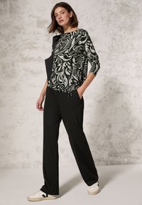 Langärmliges Oberteil mit schwarz-weißem Muster, kombiniert mit schwarzen Hosen und weißen Sneakern. Glatter Stoff mit lässiger Passform und seitlichen Taschen.