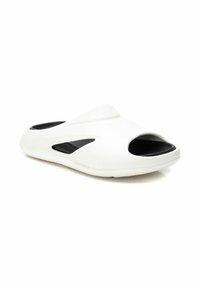 Zapato blanco sin cordones con punta abierta y interior negro, con acentos recortados y una textura suave y brillante.