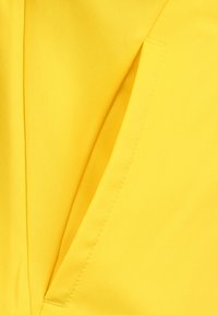 Tessuto giallo con una superficie testurizzata, dotato di una tasca laterale visibile e cuciture pulite lungo i bordi.