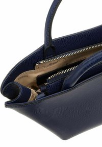 Sac à main texturé bleu marine avec deux poignées, compartiments zippés et une doublure intérieure claire en contraste. Présente des accents matériels élégants.