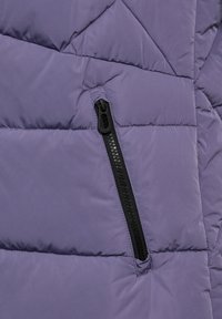 Dünne Jacke in sanftem Lavendel mit gestepptem Muster. Verfügt über eine schwarze, mit Reißverschluss gesicherte Tasche auf der Vorderseite für sichere Aufbewahrung.