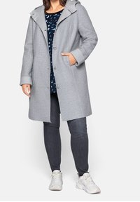 Grijze wollen jas met een capuchon, textuurstof, drie knopen en zijzakken, gecombineerd met een blauw patroon top en donkere jeans.