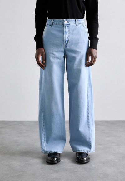 Jean large bleu clair en denim. Il présente une taille haute, un design classique à cinq poches et une fermeture éclair avec un bouton unique.