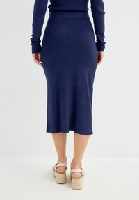 Falda midi de punto acanalado en navy con cintura ajustada, con un largo hasta media pantorrilla y una abertura en la parte posterior. Combinada con sandalias de plataforma en beige.