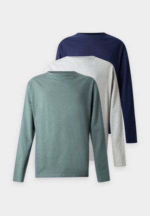 To personer iført matchende marineblå sweatshirts og løse mørkegrå jeans står side om side mod en hvid baggrund.