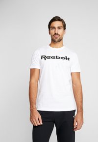 Hvitt bomull T-skjorte med et stort svart Reebok-logo over brystet. Korte ermer og rund hals.