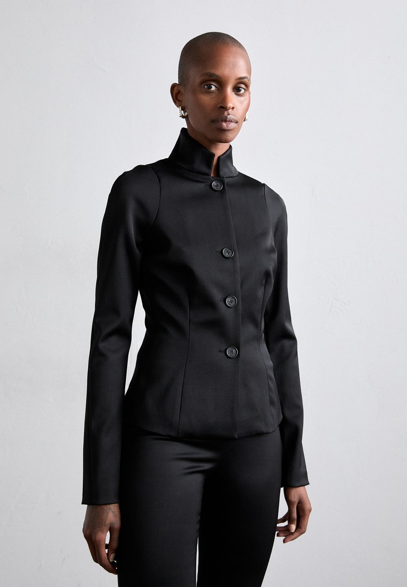 Black fitted blazer with a high collar and five large buttons. Made from smooth fabric, featuring long sleeves and a tailored silhouette.