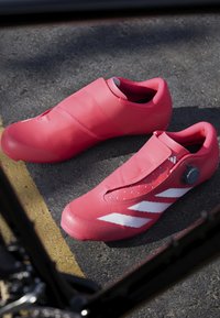 Różowe buty rowerowe o gładkiej teksturze, z rzepem, pokrętłem do regulacji i trzema białymi paskami po bokach.