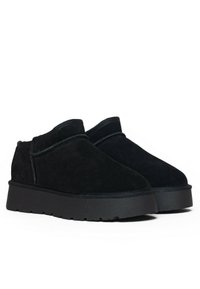 Botas de tobillo de ante negro con una suela de goma negra gruesa y un detalle de costura mínimo. Diseño de punta redonda con textura suave.