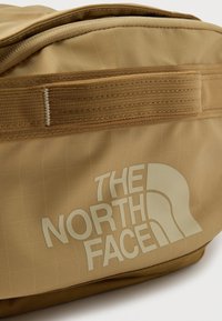 Ταν ορθογώνια τσάντα με στιβαρή επάνω λαβή και το λογότυπο "The North Face" σε μεγάλα, ανοιχτόχρωμα γράμματα μπροστά.