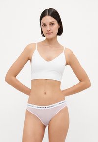 Balta bezšuvju bralette ar V veida kaklu un plānām siksnām, saskaņota ar rozā un baltajiem svītrainajiem bikini apakšbiksēm ar logotipa jostu.