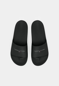 Sorte sandaler i glat materiale med en bred rem, der har "TOMMYJEANS" logo og et lille rødt og hvidt emblem.