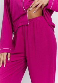 Conjunto de loungewear de color fucsia con ribetes que incluye mangas largas, un color brillante, detalles de botones y una cinturilla elástica para mayor comodidad.