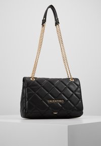 Borsa a tracolla in pelle trapuntata nera con tracolle in oro e logo dorato. Presenta una chiusura a pattina e una finitura lucida.